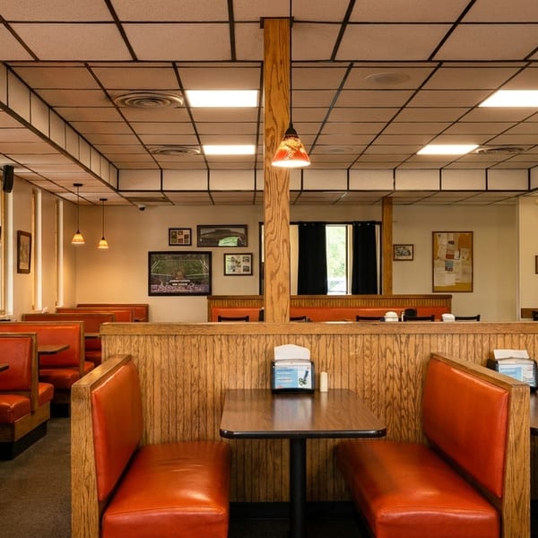 Empty diner interior with orange booths, wood paneling, and framed pictures on light walls.